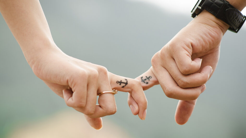 Couple holding their fingers with a tattoo of an anchor.