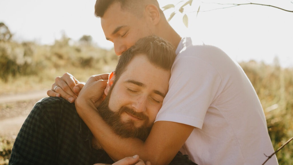 A male couple shares an intimate moment at a park.