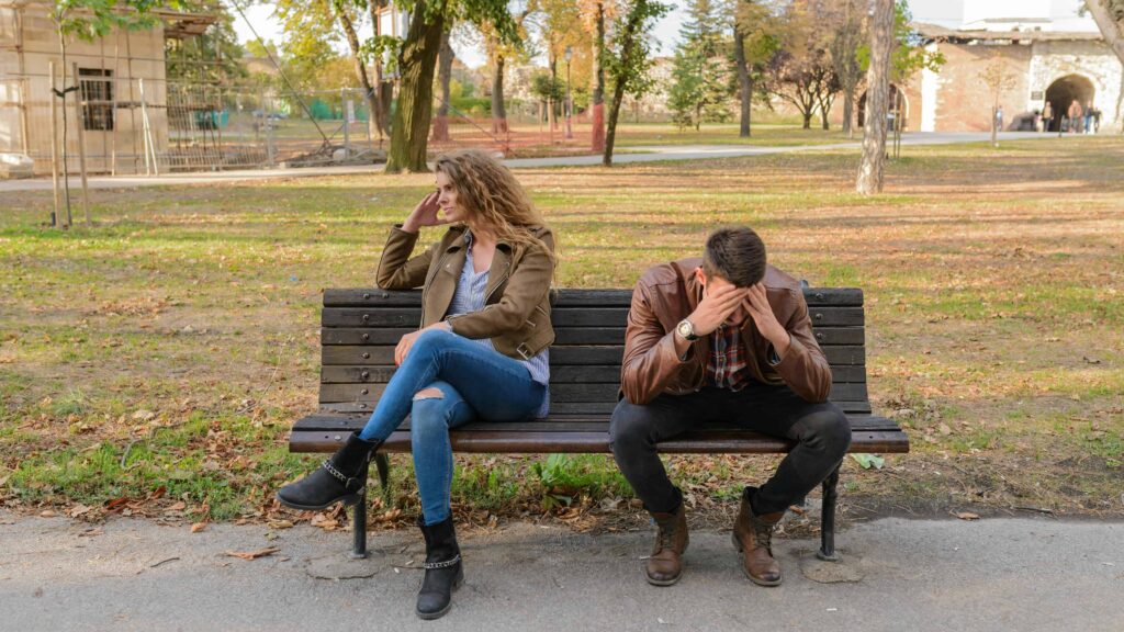 Stressed out couple sitting on a bench at a park. From the article: "how to be with someone with a disorganized attachment style"