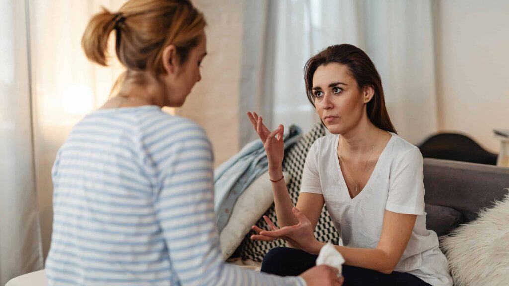 Two friends speaking in the living room. From the article: "Is people pleasing a form of manipulation?"