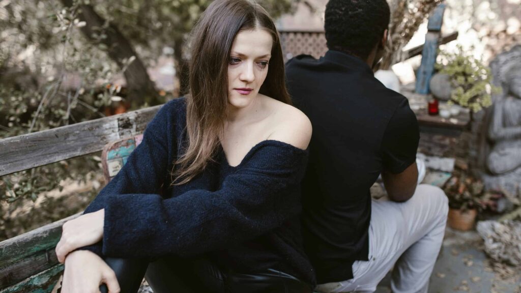 Couple sitting on a bench, upset with each other. From the article: Where does people pleasing come from?