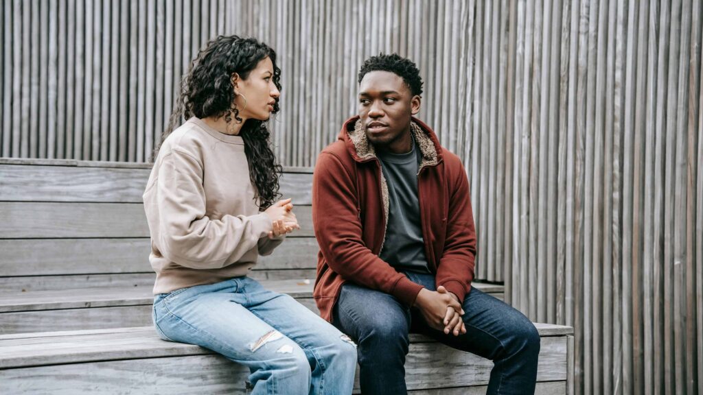 A couple having a conversation sitting on a bench. From the article: adhd and people pleasing.