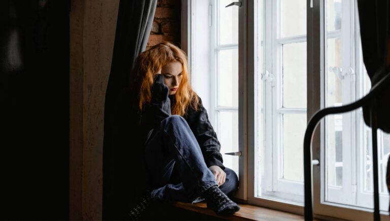 Woman feeling anxious sitting on a window from the article "Relationship OCD"