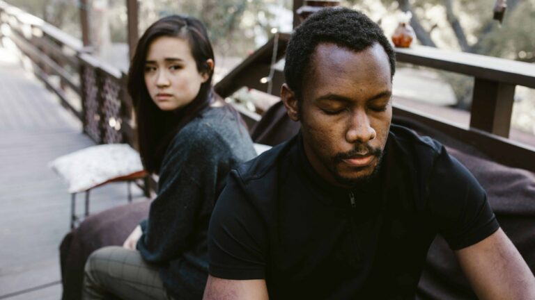 A couple distant with each other sitting on a beach. From the article "How to heal avoidant attachment style"